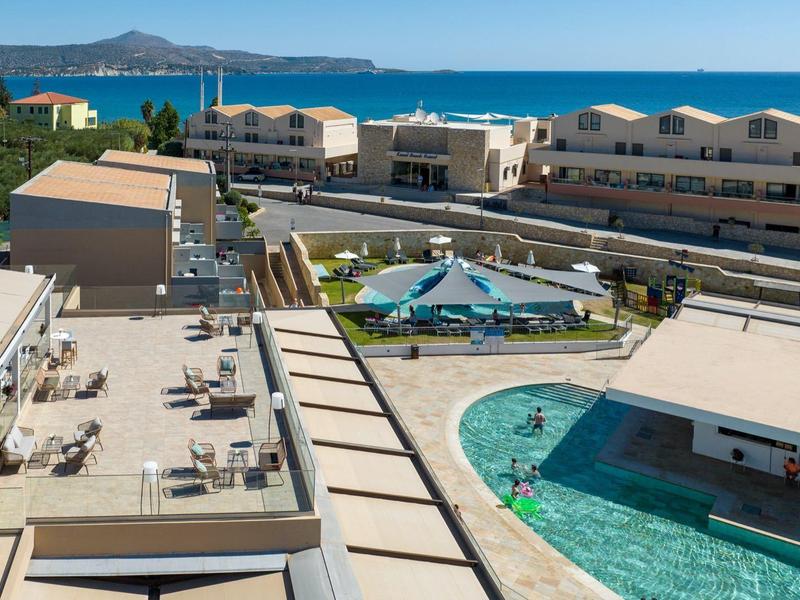 Hotelový bazén s lehátky, slunečníky a výhledem na oceán za jasné oblohy.