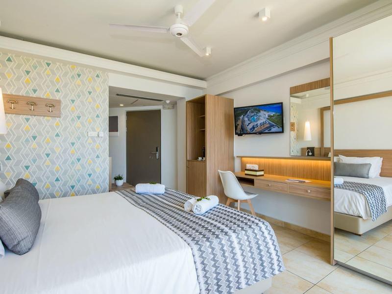 Světly hotelový pokoj s manželskou postelí, vzorovanou tapetou a televizí na zdi.