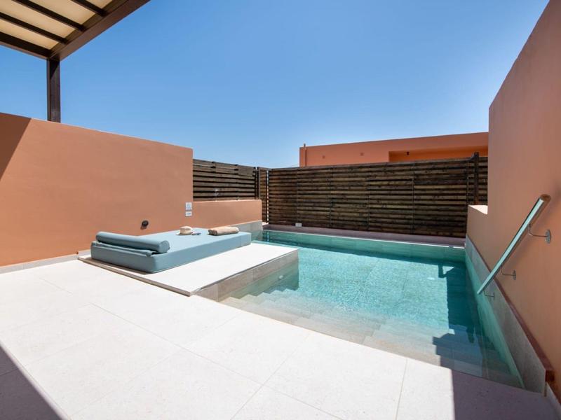 Malý venkovní bazén se světle modrou vodou, obklopený broskvovými zdmi a bílými dlaždicemi.