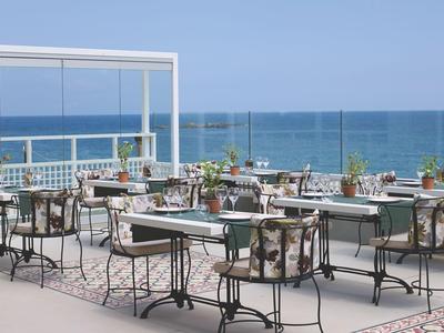 Terrasse mit Tischen und Stühlen mit Meerblick an einem sonnigen Tag.