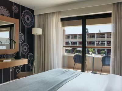 Modernes Hotelzimmer mit großem Bett, Balkon und Blick auf eine Außenanlage.