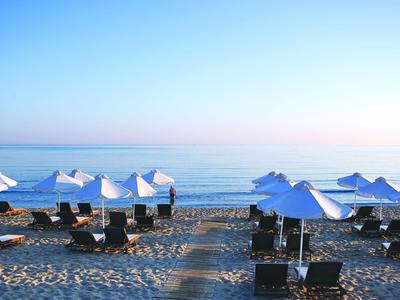 Strand mit Sonnenliegen und weißen Sonnenschirmen bei ruhigem Meer und klarem Himmel.