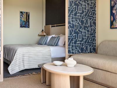 Gemütliches Hotelzimmer mit Bett, kleinen Tischen und Couch in neutralen Farben.