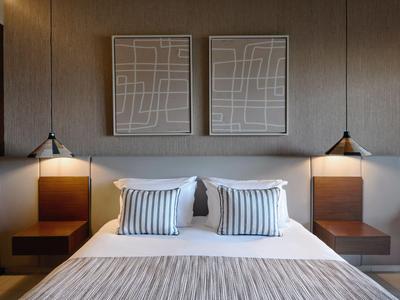 Habitación de hotel moderna con cama doble, cojines a rayas y arte geométrico en la pared sobre el cabecero.