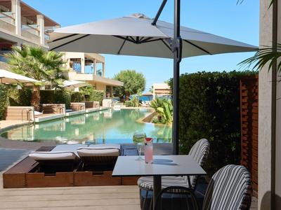 Blick auf einen Poolbereich mit Liegestühlen und Sonnenschirmen in einem Hotel bei klarem Himmel.