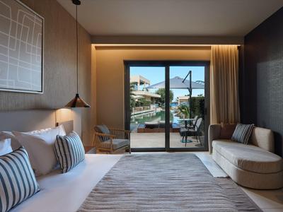 Modernes Hotelzimmer mit großem Bett, Sofa, Teppich und Blick auf Terrasse durch Glasschiebetür.