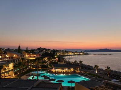 Hotel con piscina iluminada y vista al mar al atardecer.
