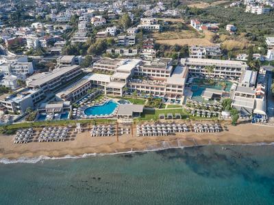 Vista aérea de un hotel en la playa con piscina, tumbonas y agua clara.
