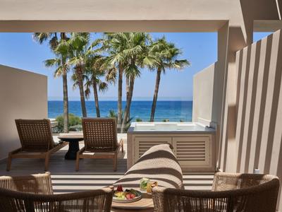 Vista desde una terraza con sillas hacia palmeras y el mar bajo cielo despejado.