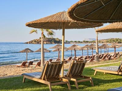 Strand mit Liegestühlen und Sonnenschirmen aus Stroh am Meer bei klarem Himmel.