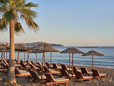 Leerer Strand mit Liegestühlen, Sonnenschirmen und Palmen bei Sonnenuntergang.