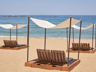 Drei schattige Strandliegen mit weißen Sonnensegeln am Sandstrand vor ruhigem Meer.