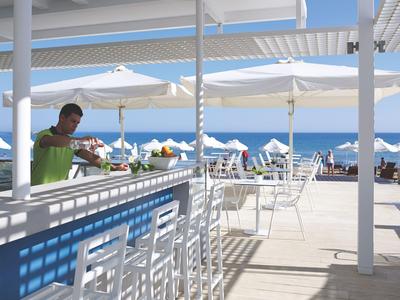 Moderner Außenbereich einer Bar mit weißen Stühlen und Blick auf das Meer unter Sonnenschirmen.