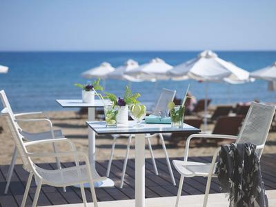 Tisch mit Drinks und Stühlen am Strand mit Sonnenschirmen und Meer im Hintergrund