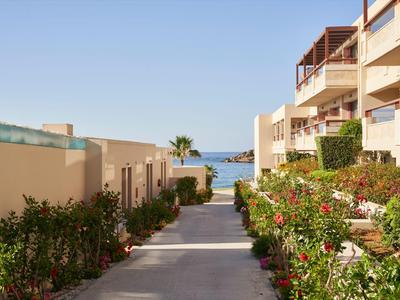 Weg zwischen Hotelgebäuden mit Blumen zu einem Meerblick unter blauem Himmel.