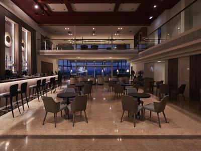 Eleganter Hotel-Loungebereich mit Tischen, Stühlen und Bartresen unter warmen Deckenleuchten.