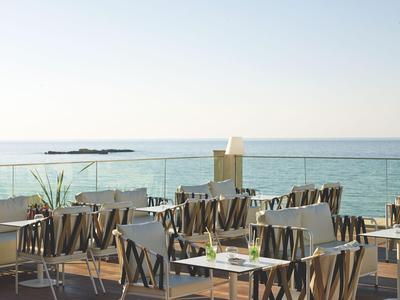 Terrasse eines Hotels mit Tischen und Stühlen mit Blick aufs Meer und blauen Himmel