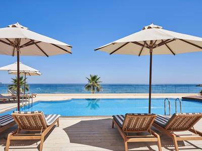 Poolbereich mit Liegestühlen und Sonnenschirmen mit Blick auf das Meer bei klarem Himmel