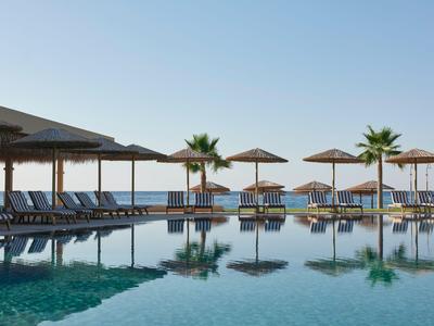 Moderner Poolbereich mit Liegestühlen und Sonnenschirmen, Palmen und Meerblick bei klarem Himmel.