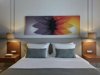 Modernes Hotelzimmer mit Doppelbett, farbenfrohem Wandbild und zwei Hängelampen.