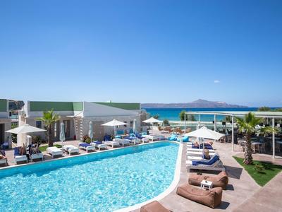 Großer Außenpool mit Liegestühlen und Sonnenschirmen, klarer Himmel und Meer im Hintergrund.