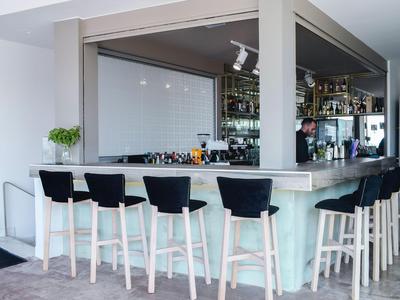 Moderner Hotelbarbereich mit hoher Theke und schwarzen Barhockern in hellem Ambiente.