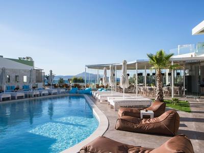 Moderner Außenpoolbereich mit Sonnenliegen und einem Restaurant bei klarem Himmel.