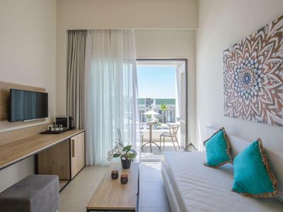 Modernes Zimmer mit Doppelbett, türkisen Kissen, TV, Sideboard und Balkon mit Sitzgelegenheit.