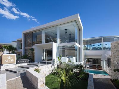 Modernes, zweistöckiges Haus mit großflächigen Glasfronten, weißer Fassade und grünem Vorgarten.