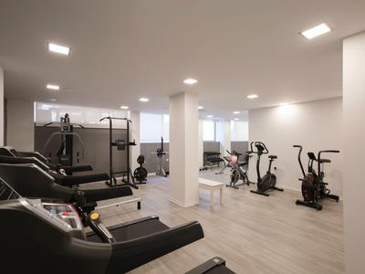 Moderner Fitnessraum mit Laufbändern, Crosstrainern und Gewichten in hellem Raum.