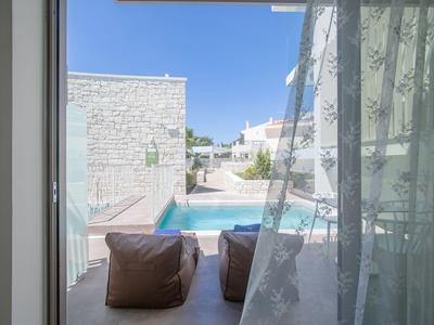 Blick durch ein Fenster auf einen Poolbereich mit braunen Sitzsäcken und weißen Gebäuden.
