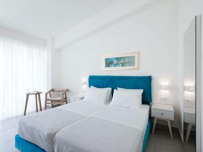 Helles Schlafzimmer mit großem Bett, blauem Kopfteil, weißen Wänden und minimaler Einrichtung.