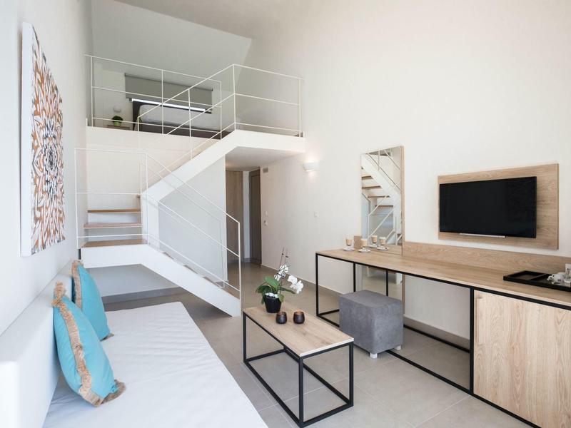 Helles Zimmer mit weißer Wand, Holzarbeitsplatz, Couch, Treppe zur Galerie und Wandbild.