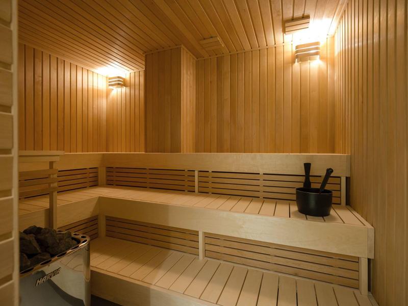 Holzsauna mit mehrstöckigen Sitzbänken, Eimer und Aufgusskelle, warmes Licht.