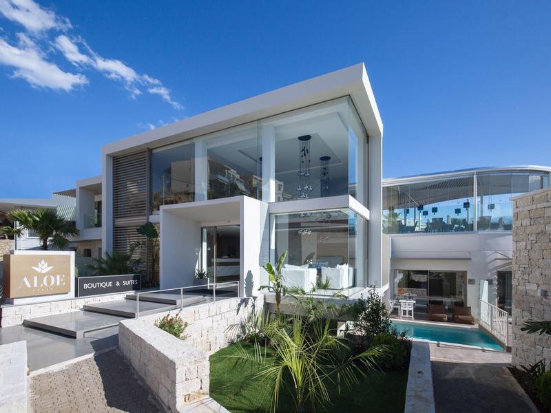 Modernes, zweistöckiges Haus mit großflächigen Glasfronten, weißer Fassade und grünem Vorgarten.