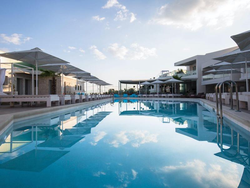 Großer Außenpool mit klarem Wasser zwischen modernen Gebäuden und Sonnenschirmen bei Tageslicht.