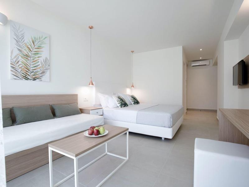 Moderner, heller Raum mit Sofa, Doppelbett, Tisch und minimalistischer Dekoration in Weiß- und Grautönen.