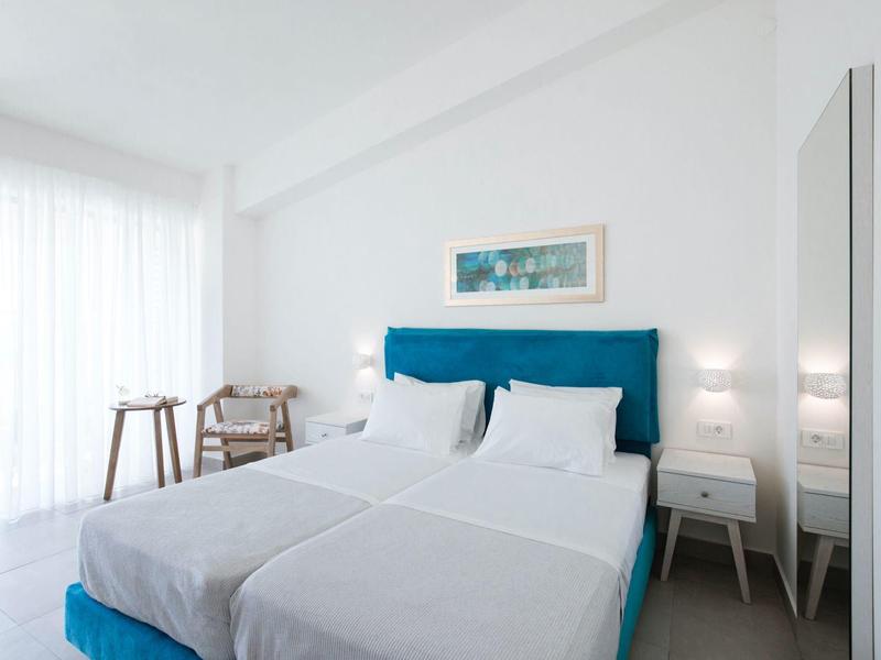 Helles Schlafzimmer mit großem Bett, blauem Kopfteil, weißen Wänden und minimaler Einrichtung.