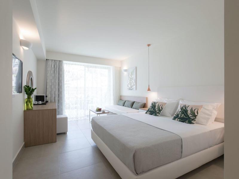 Hell eingerichtetes Schlafzimmer mit großem Doppelbett, weißen Wänden und Fenster mit Vorhängen.