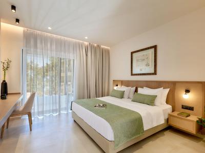 Habitación de hotel moderna con cama grande, ropa de cama verde y blanca, escritorio y balcón con cortinas.