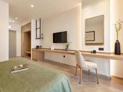 Modernes Hotelzimmer mit langem Holzschreibtisch, Stuhl, Fernseher und grün bezogenem Bett.