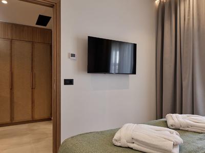 Modernes Hotelzimmer mit Wand-TV, Garderobe und Betten mit weißen Handtüchern.