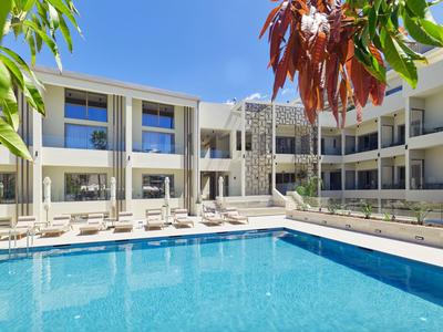 Moderner Hotelpool umgeben von zweistöckigen Gebäuden und Sonnenliegen bei klarem Himmel.