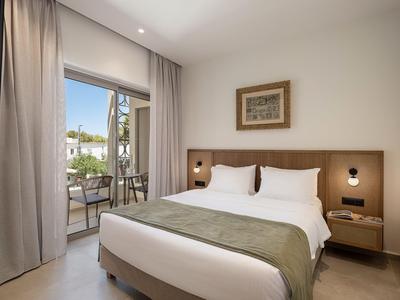 Geräumiges Hotelzimmer mit großer Bett, Wandlampen und Balkon mit Außenmöbeln.