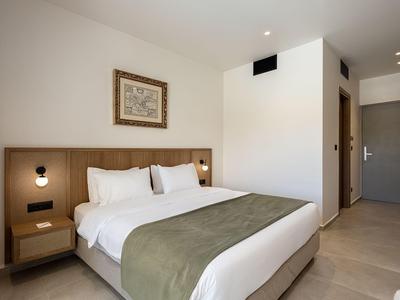 Schlichter, moderner Hotelzimmer mit großem Bett, Holzlattenkopfteil und minimaler Dekoration.