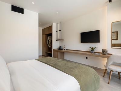 Helles Hotelzimmer mit großem Bett, Fernseher an der Wand und Schreibtisch mit Stuhl.