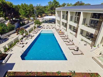 Moderner Hotelpool mit Liegestühlen und grüner Umgebung bei klarem Himmel.