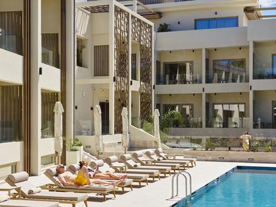 Moderner Hotelpoolbereich mit Sonnenliegen und Gästen, umgeben von einem mehrstöckigen Gebäude.