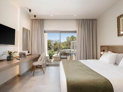 Modernes Hotelzimmer mit großem Bett, Schreibtisch, Fernseher und Balkon mit Blick ins Grüne.