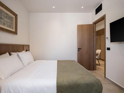 Helles Hotelzimmer mit großem Bett, weißen Wänden und offenem Holztür zur Lounge.